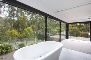 A modern bathroom with a freestanding bathtub, large windows, and a view of a forested area.