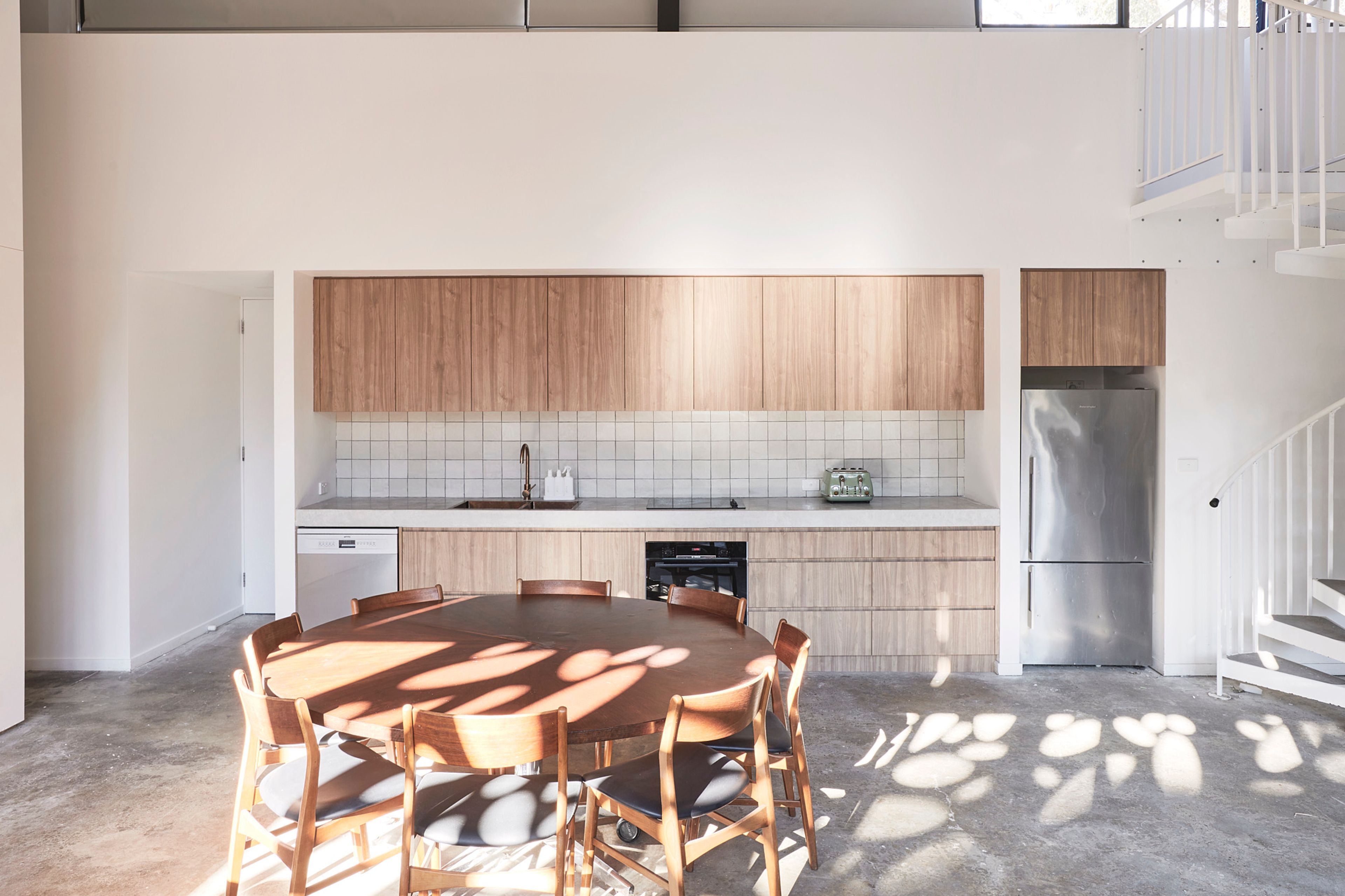 Une cuisine moderne avec des meubles en bois, un réfrigérateur en acier inoxydable et une table à manger avec des chaises.