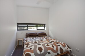 A small, single-bed room with a window, a small stool, and a patterned bedspread. - The Shed Great Ocean Road (Lorne)