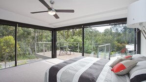A bedroom with a large bed, a ceiling fan, and a view of a balcony with outdoor furniture.