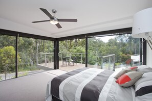 A bedroom with a large bed, a ceiling fan, and a view of a balcony with outdoor furniture.