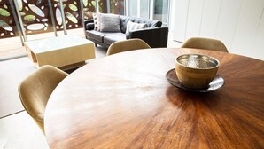 A round wooden dining table with a woven bowl on a saucer, surrounded by four chairs.