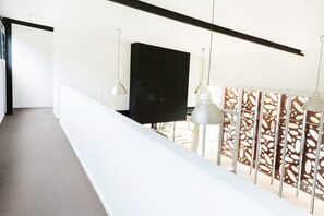 A modern interior with a white balcony railing, a flat-screen TV mounted on the wall, and pendant lights. - The Shed Great Ocean Road (Lorne)