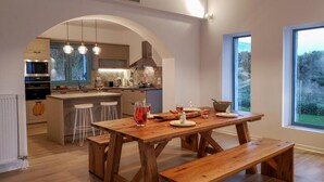 A modern kitchen with an island, wooden benches, and a dining table set for four. - Exclusive Sea View Villa Madelaine (SPARTIA)