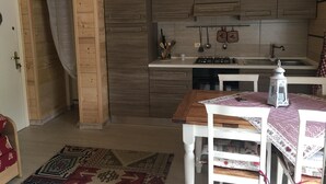 A kitchen with wooden cabinets, a stove, and a sink. There is a table with a tablecloth and a chair. - House in the center of Ponte di Legno (Ponte di Legno)