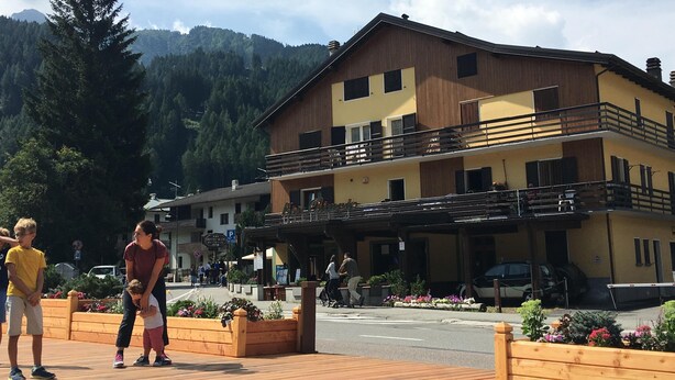 A multi-story building with a balcony, surrounded by a wooden deck and flower beds. - House in the center of Ponte di Legno (Ponte di Legno)