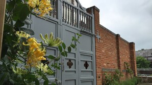 A grey metal gate with a decorative metal fence, a brick wall, and a bench in the background.