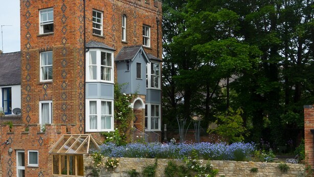 A traditional brick building with a stone wall and a small garden with flowers.