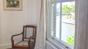 Ein Teil eines Raumes mit einem Holzstuhl, einem Fenster mit Vorhängen und einem gerahmten Bild an der Wand.