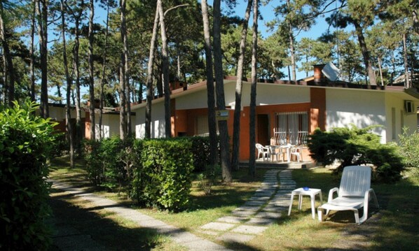 A bungalow with a patio, surrounded by trees and greenery.
