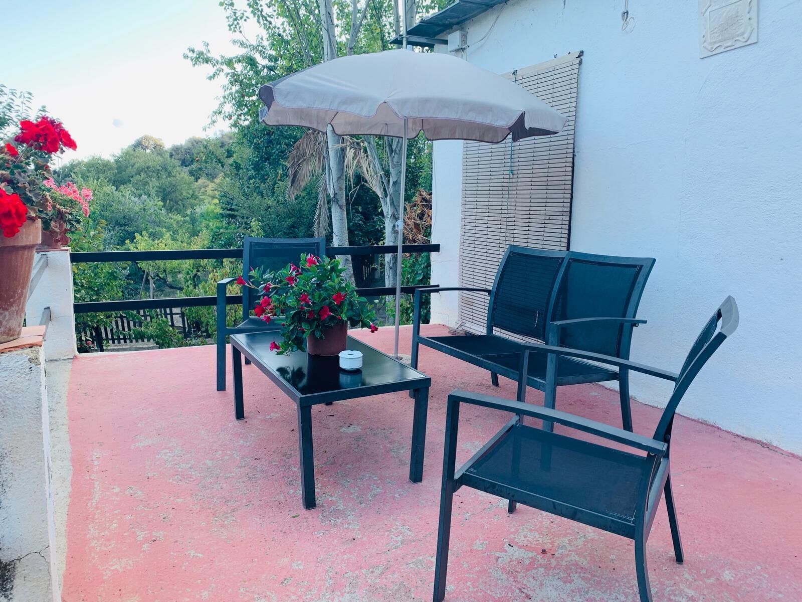 An outdoor patio with a table, two chairs, a potted plant, and a hanging umbrella.