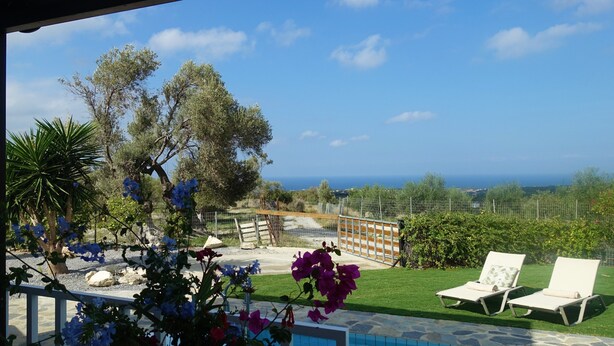 A poolside area with a view of the sea, surrounded by greenery and a fence. - Beautiful quiet villa (4p), private pool and great sea views (Kirianna)