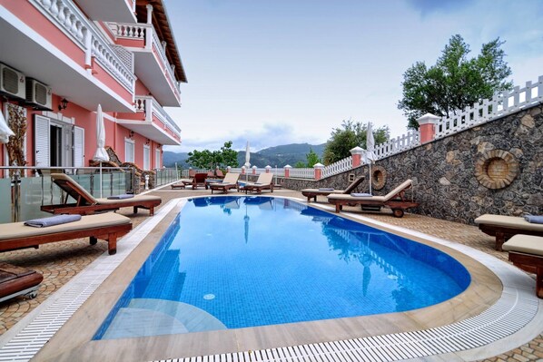 A swimming pool with lounge chairs and a stone wall. - Angela Pool Apartment Agios Georgios (Ag. Georgios Pagon)