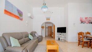 Een woonkamer met een bank, een salontafel, een televisie en een eethoek met stoelen.