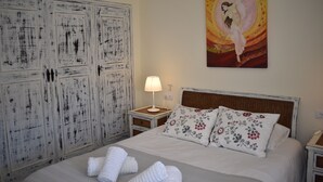 Quarto com cama, almofadas, mesa de cabeceira, luminária e guarda-roupa.