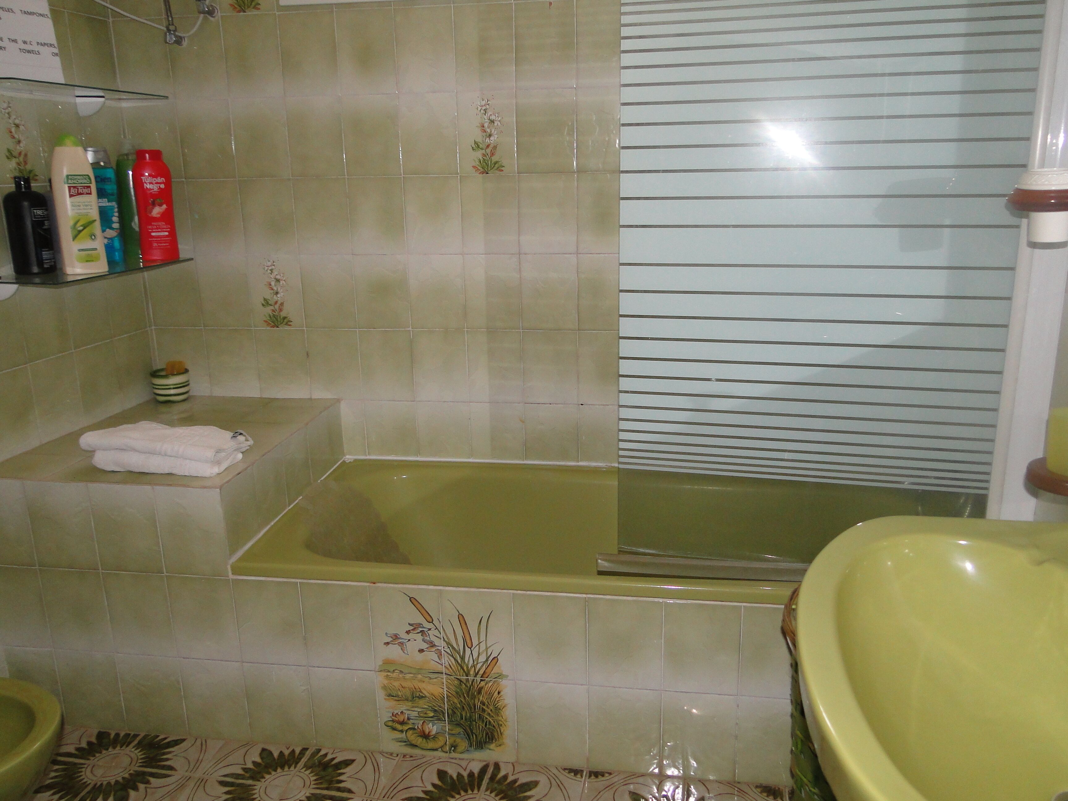 A bathroom with a bathtub, a toilet, and a sink. There are toiletries on a shelf, and a towel is folded on the edge of the tub.
