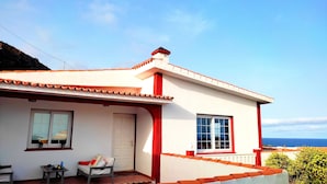 Una casa costera con fachada blanca y detalles rojos, que cuenta con un balcón con vista al mar.