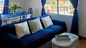 Una habitación con un sofá azul, una mesa de comedor y vistas al exterior.
