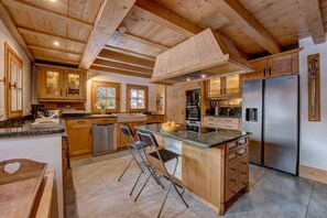 A spacious kitchen with wooden cabinetry, a central island with seating, and a stainless steel refrigerator.