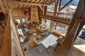 A wooden cabin interior with a cozy living area, a fireplace, and large windows offering a view of the surrounding landscape.