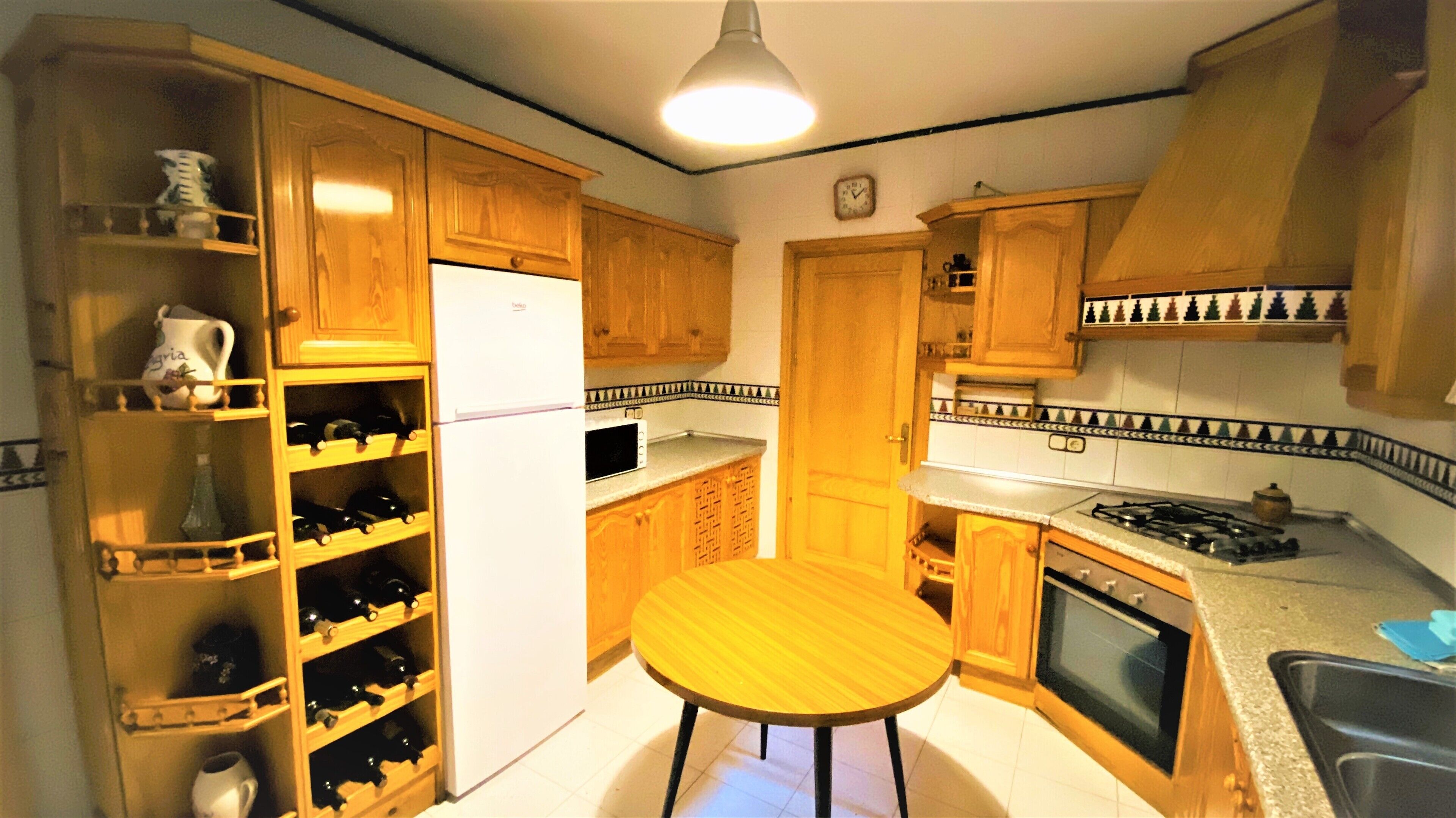 A compact kitchen with wooden cabinets, a built-in wine rack, a refrigerator, a microwave, a stove, and a sink.