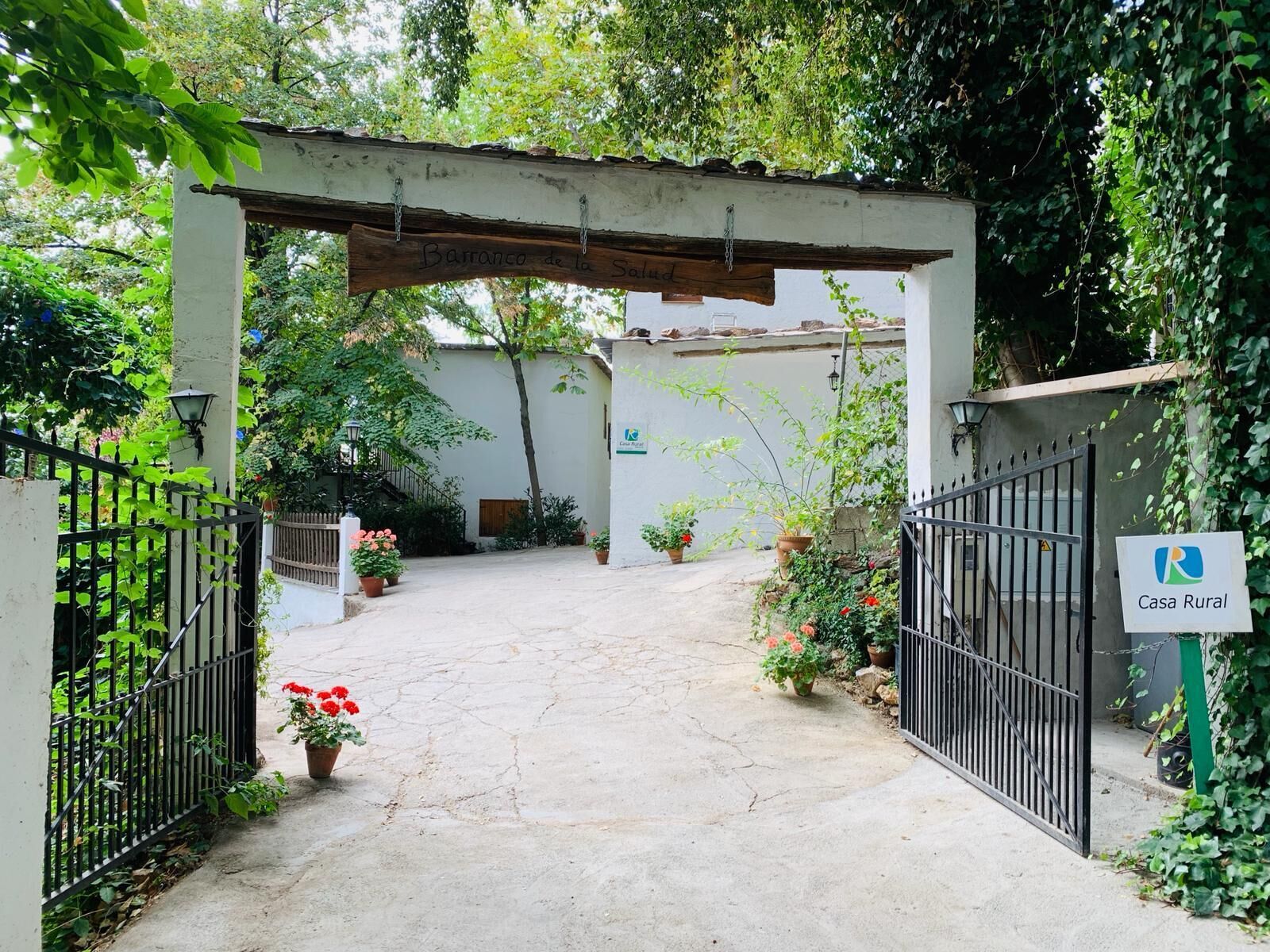 A gated entrance to a property named Casa Rural, featuring a rustic archway and a paved pathway leading to a white building.