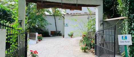 A gated entrance to a property named Casa Rural, featuring a rustic archway and a paved pathway leading to a white building.