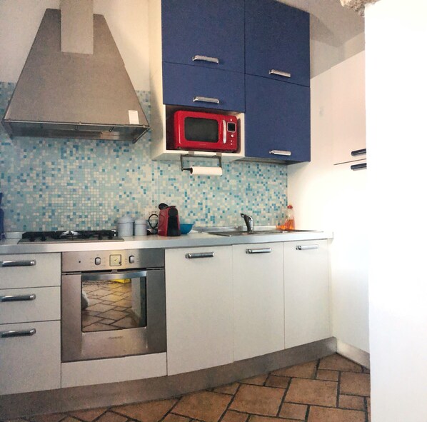 Una cocina con armarios blancos, un microondas rojo, una estufa a gas y un salpicadero de azulejos.