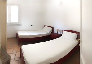 A bedroom with two single beds, a nightstand, a lamp, and a window. - Incanto Apartment Golfo Aranci Sardinia, front sea apartment (Golfo Aranci)