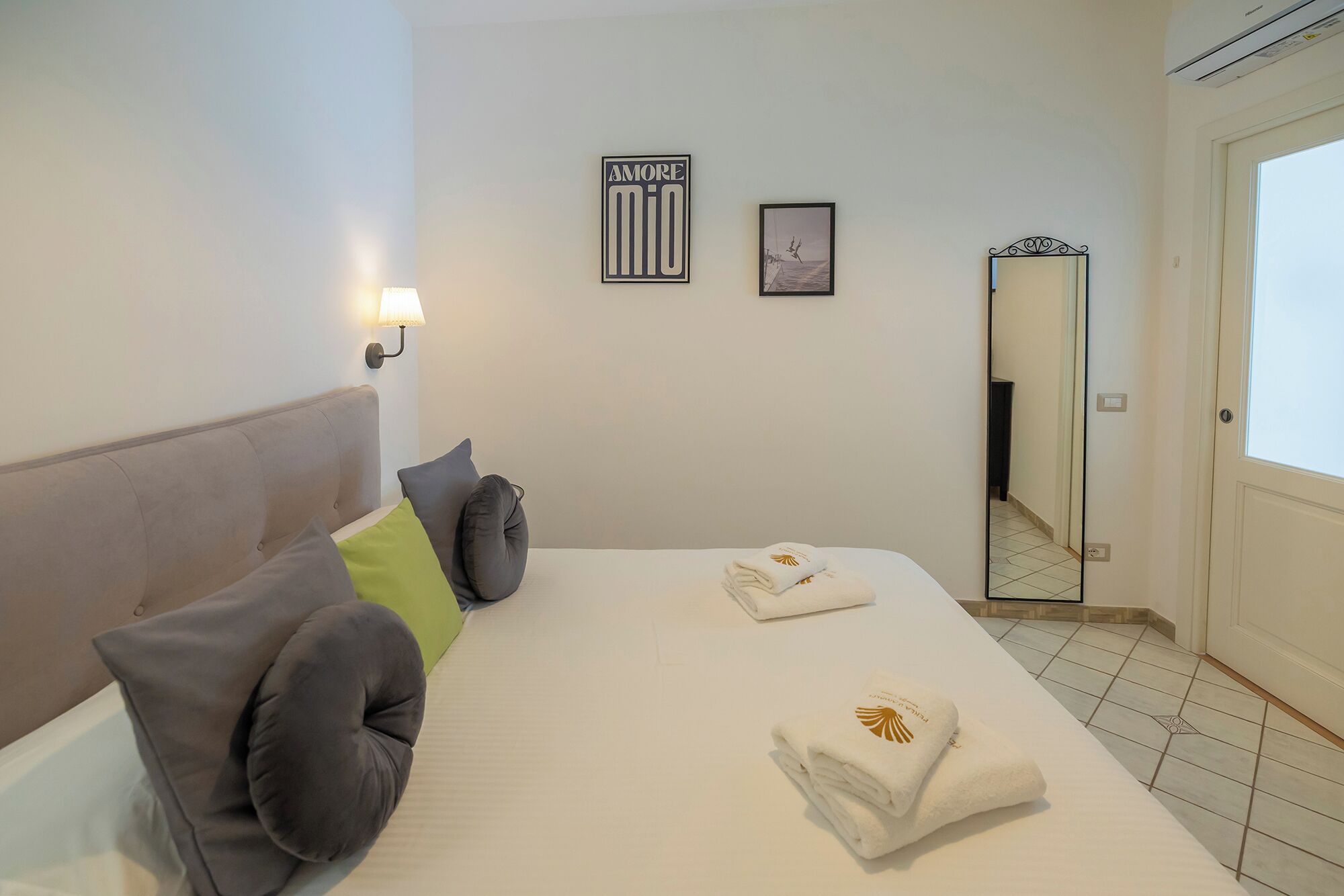 A hotel room with a bed, pillows, a wall-mounted lamp, and two framed pictures.