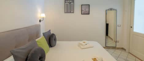 A hotel room with a bed, pillows, a wall-mounted lamp, and two framed pictures.