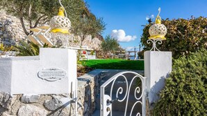 Una entrada protegida por una reja, con faroles decorativos, un muro de piedra y un cartel con información de contacto.