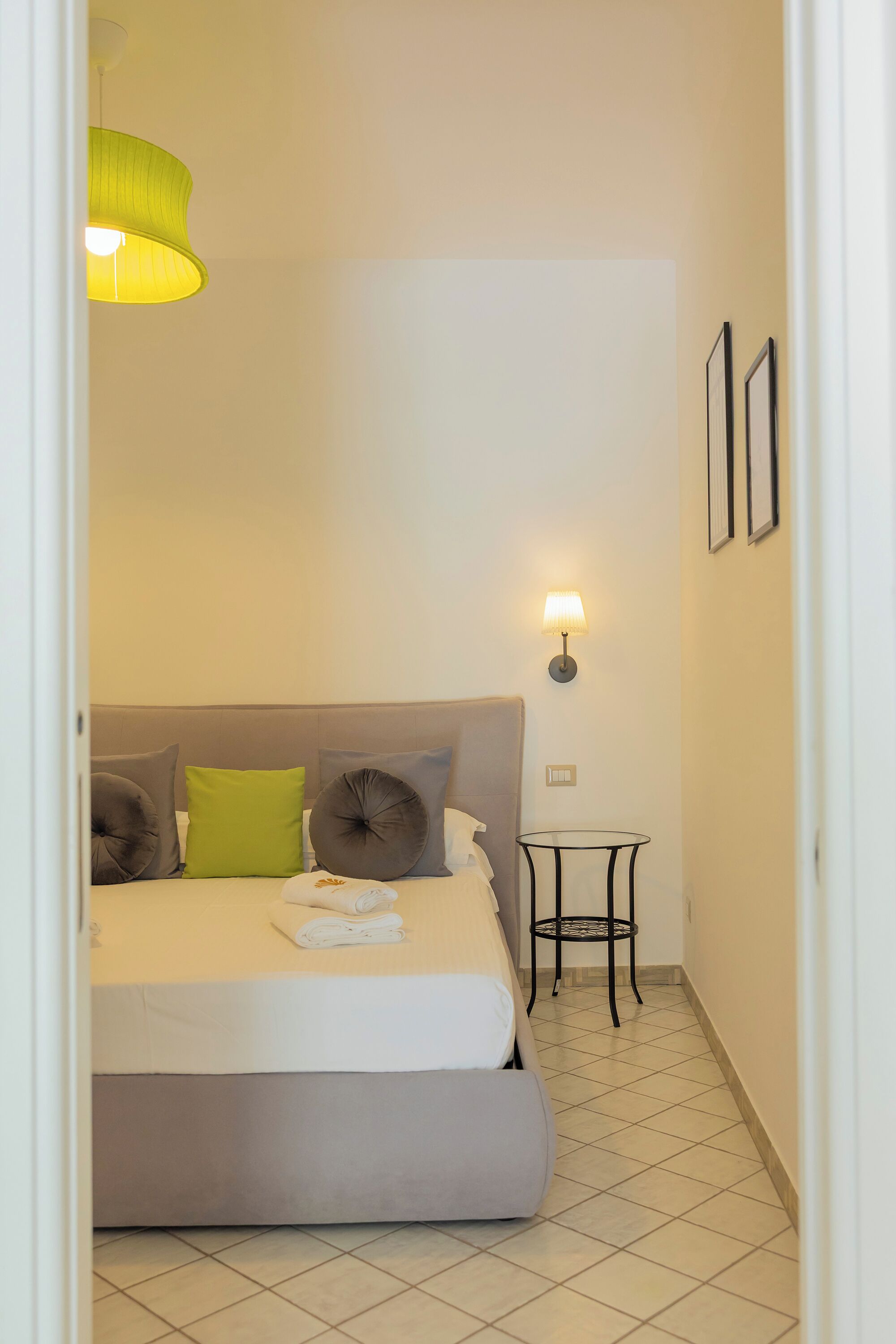 Un dormitorio con cama, almohadas, una mesita de noche, una lámpara y un cuadro en la pared.