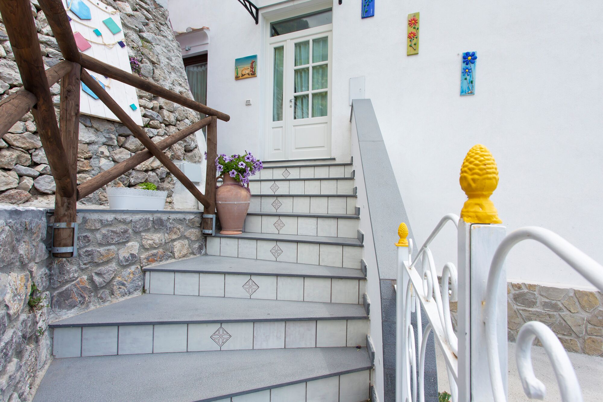 Uma escadaria com paredes de pedra, uma porta branca e um vaso de planta.