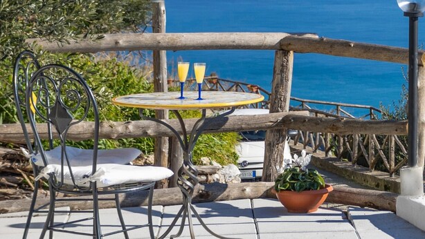 Una terraza con mesa y sillas, con vista al mar y montañas.