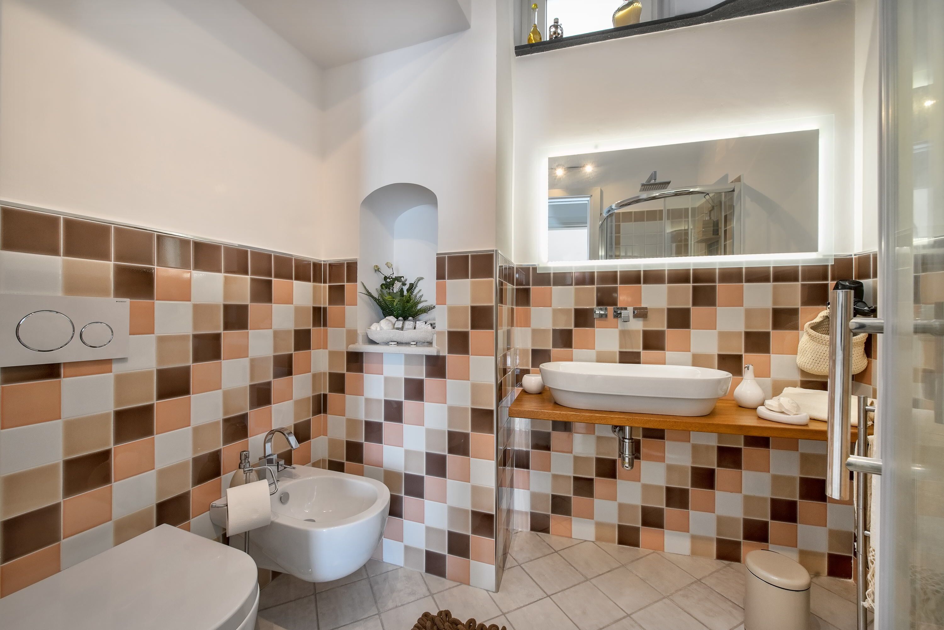 A modern bathroom with a checkered tile backsplash, a freestanding sink, a bidet, and a mirror above the sink.