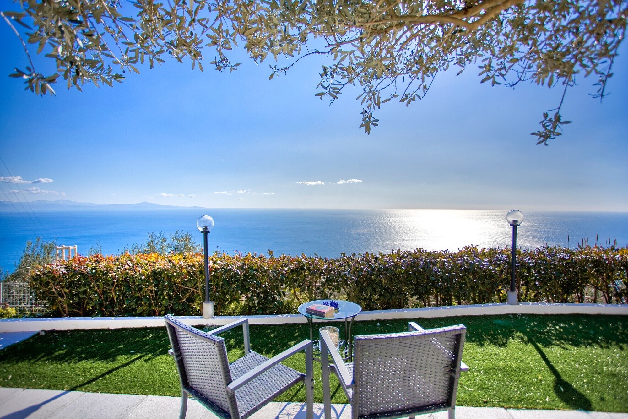 A terrace with two wicker chairs, a small round table, and a view of the sea.
