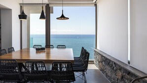 Un espace repas avec une table en bois et des chaises noires, donnant sur une étendue d’eau.