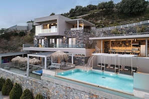 A modern multi-story building with a swimming pool, outdoor seating, and a stone facade. - Fotinari Villa II -High quality above a cozy beach (Rethymno)