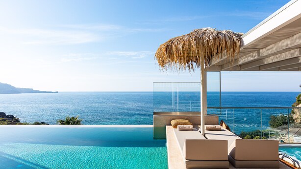 Une piscine à débordement offrant une vue imprenable sur l’océan, un espace détente agrémenté d’un parasol en chaume, et une architecture moderne.