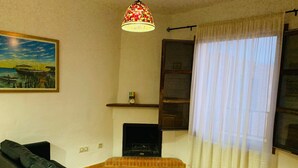 A living room with a black sofa, a fireplace, a hanging lamp, and a window with white curtains. - Self catering Barranco de la Salud for 2 people (Nevada)