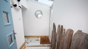 Un couloir étroit avec une porte bleue, un plancher en bois et une clôture en bois sur le côté droit.
