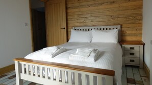 Une chambre à coucher avec une tête de lit en bois, un lit blanc avec deux oreillers, une table de chevet en bois et une commode blanche.