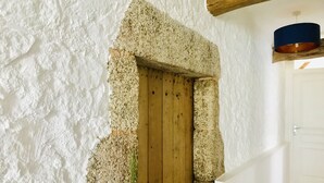 Un intérieur rustique avec une arche en pierre menant à une porte en bois, des murs blancs et un sol carrelé.