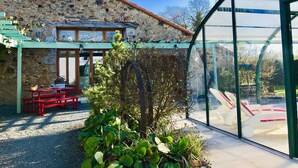 Un bâtiment en pierre surmonté d’un toit végétalisé, avec une serre en verre et un banc rouge.
