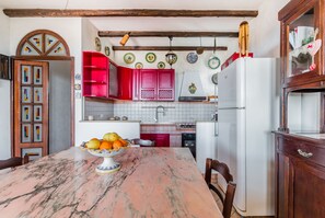 A kitchen with a marble table, red cabinets, and a white refrigerator.