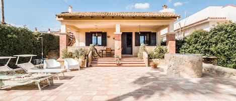 A house with a tiled patio, outdoor seating, and a staircase leading to the entrance.