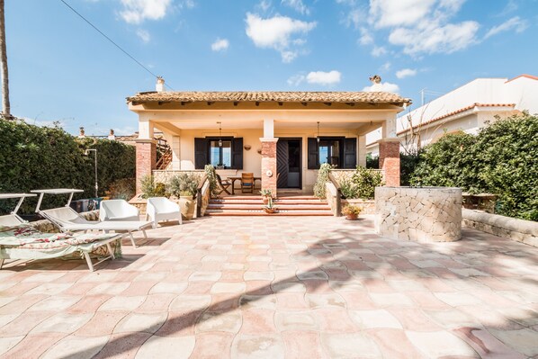 A house with a tiled patio, outdoor seating, and a staircase leading to the entrance.