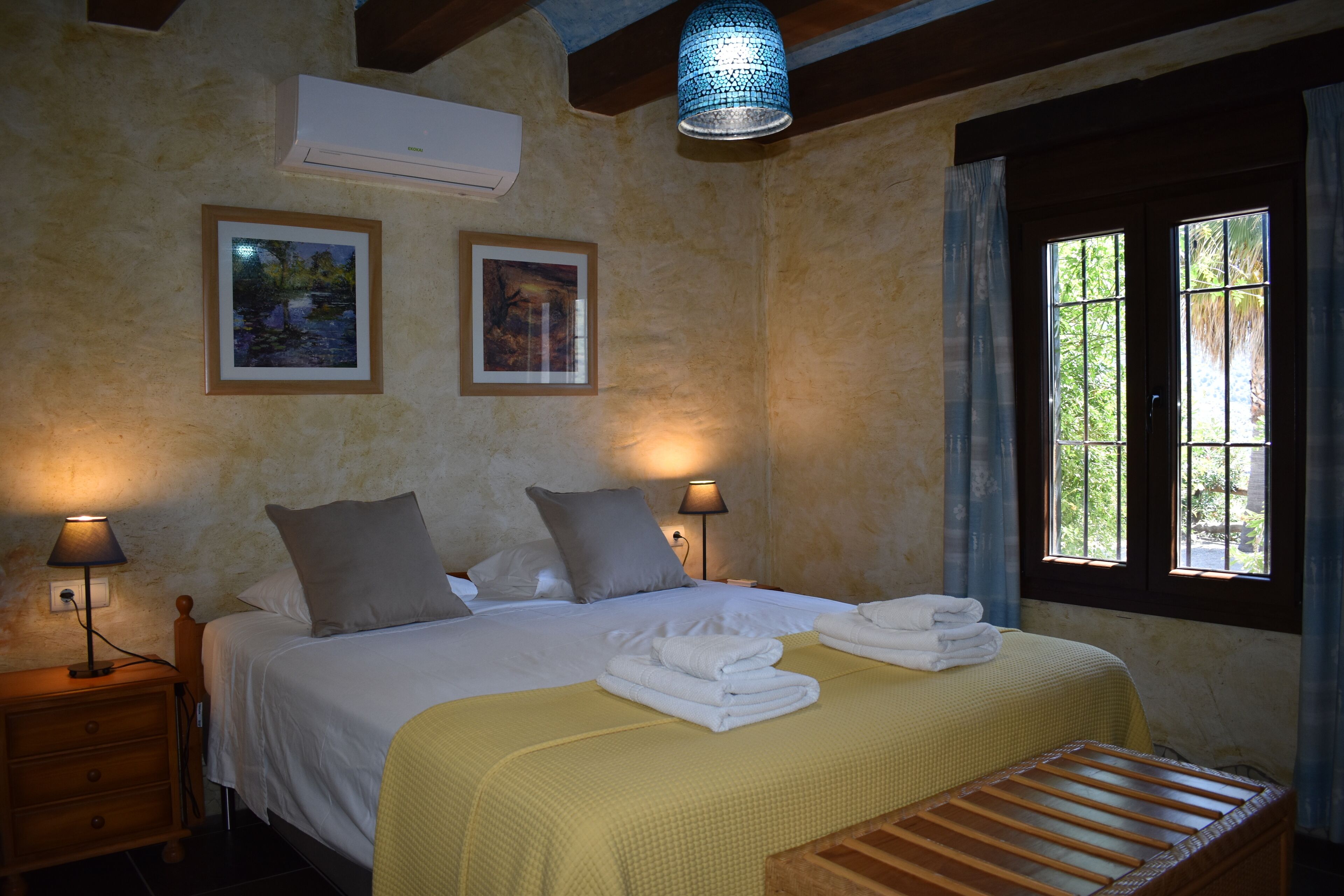 A bedroom with a bed, bedside lamps, a wooden bench, and a window with curtains.