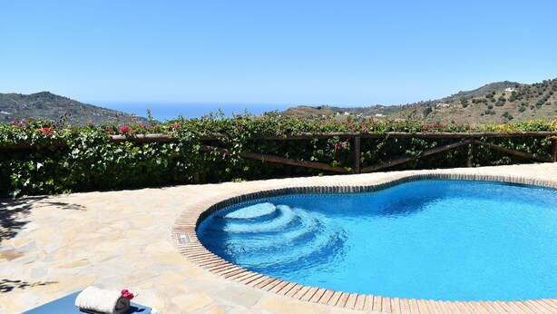 A swimming pool with a stone patio, two lounge chairs, and a wooden fence with flowers. - Finca Ortiz with private pool for 6 people and fantastic views (Cómpeta)